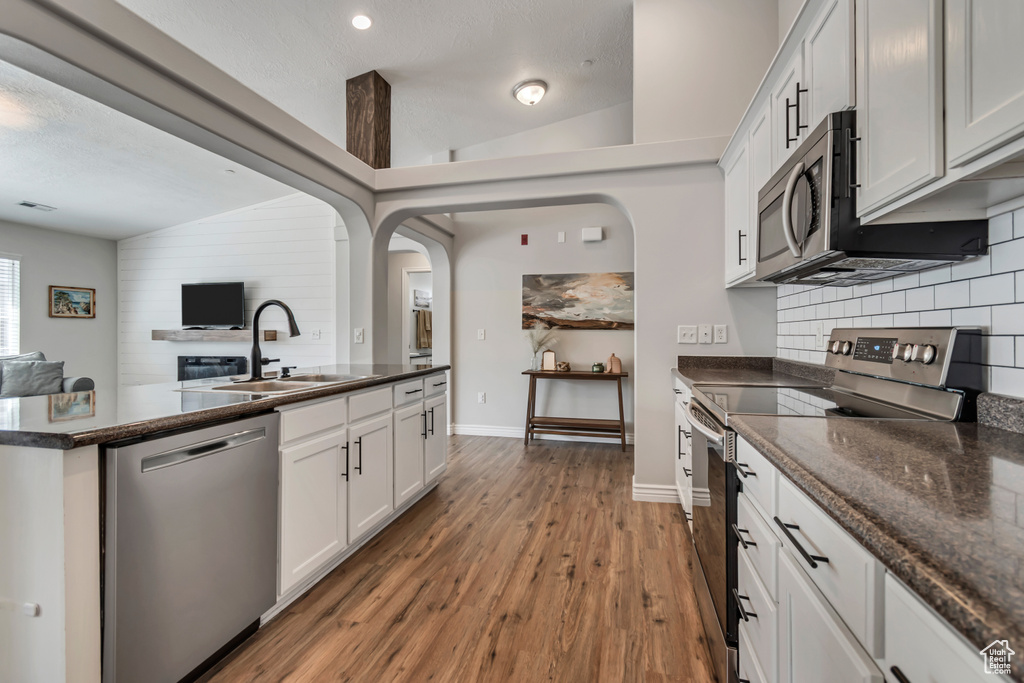 Kitchen featuring stainless steel appliances, decorative backsplash, wood finished floors, open floor plan, and white cabinets