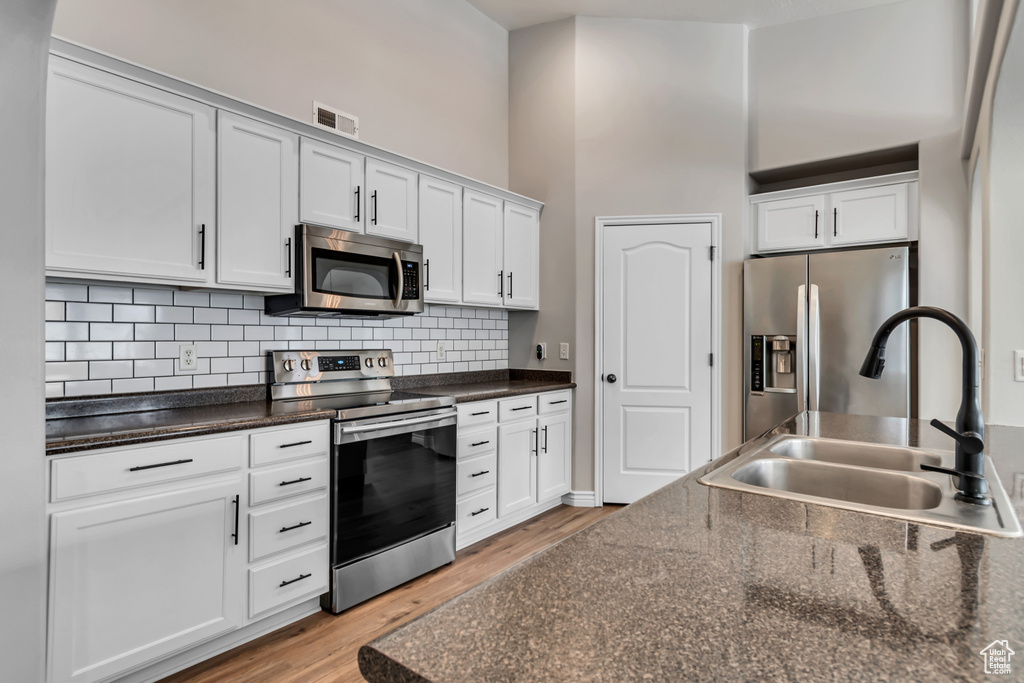 Kitchen with appliances with stainless steel finishes, light wood-style floors, tasteful backsplash, white cabinets, and a high ceiling