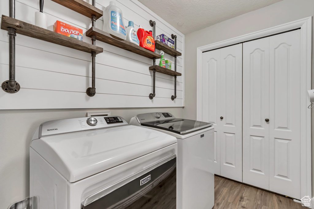 Washroom featuring washer and dryer, light wood finished floors, and a textured ceiling