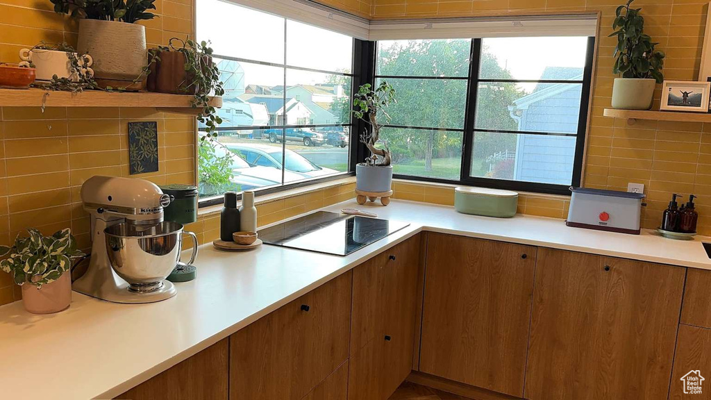 Kitchen with healthy amount of natural light, light countertops, brown cabinetry, and decorative backsplash