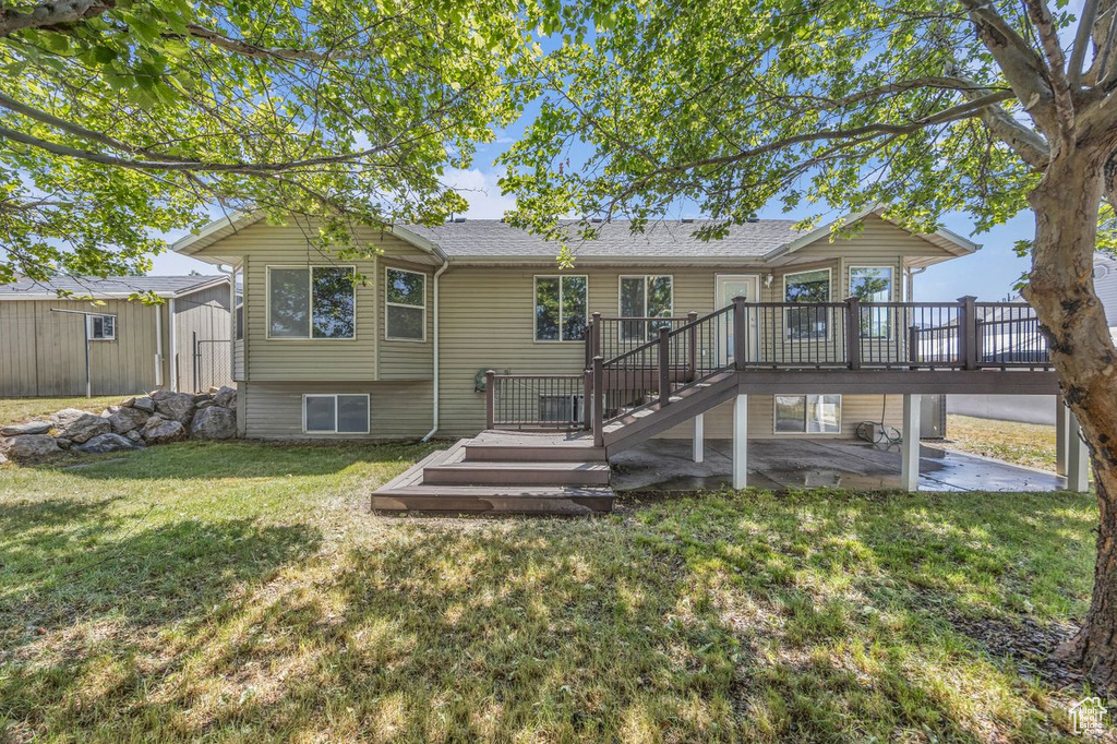 Rear view of property with a wooden deck, a patio, a lawn, a shed, and a shingled roof