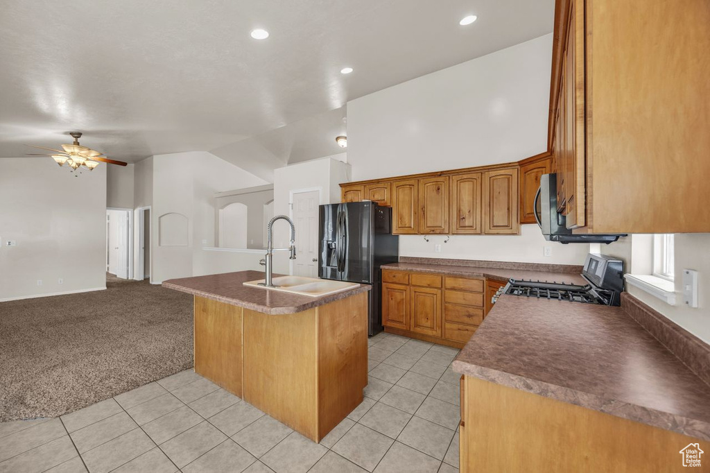 Kitchen with gas range oven, black fridge, a center island with sink, open floor plan, and ceiling fan