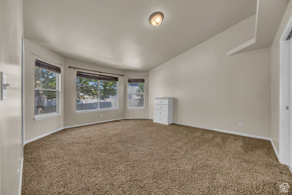 Empty room featuring carpet floors and vaulted ceiling