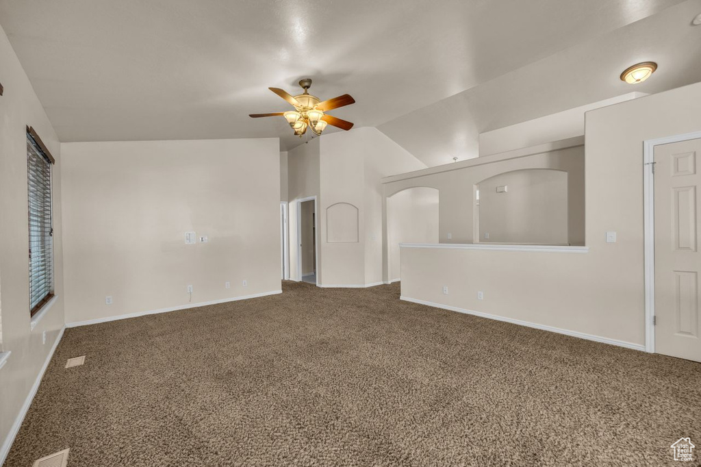 Carpeted empty room featuring a ceiling fan and vaulted ceiling