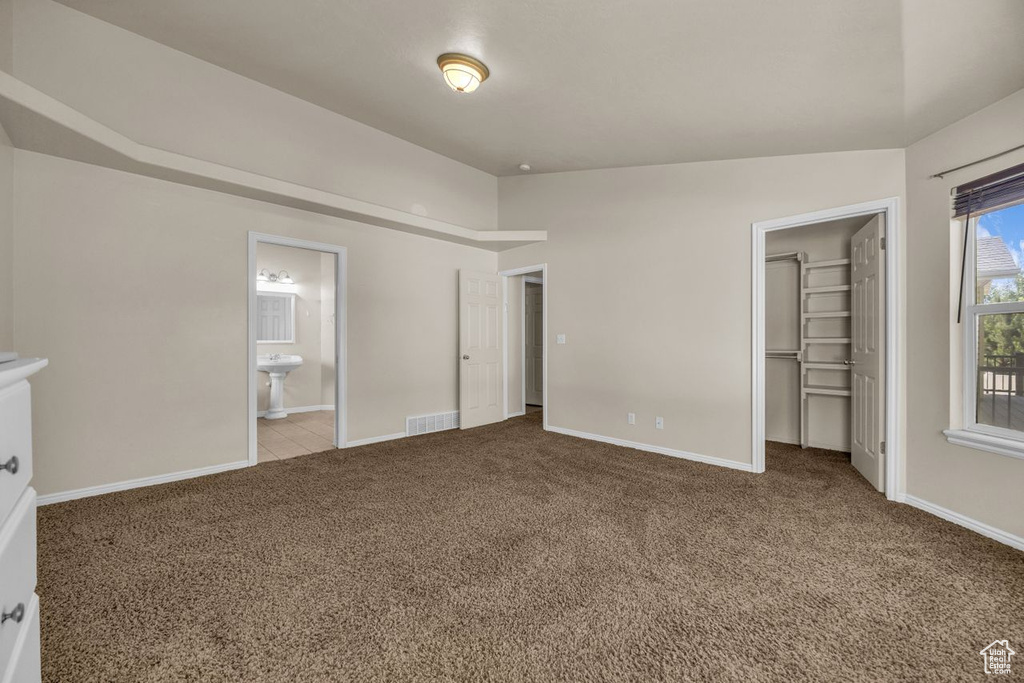 Unfurnished bedroom featuring carpet, a spacious closet, ensuite bathroom, and a closet