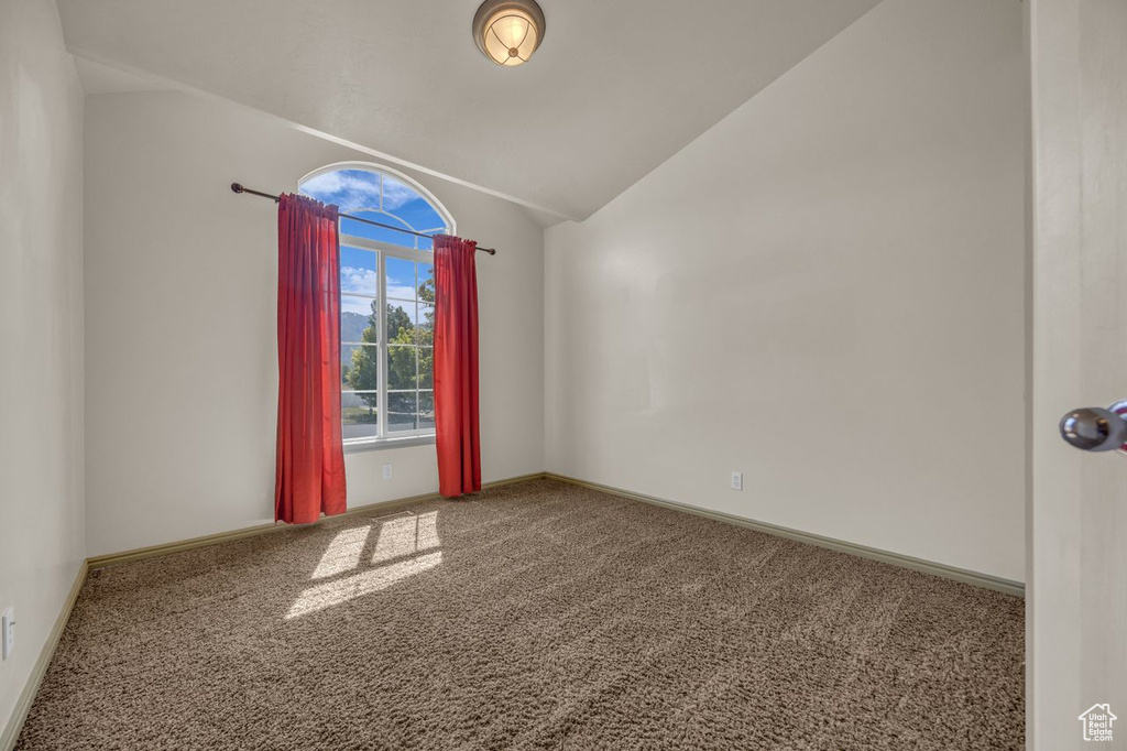 Spare room featuring carpet flooring and vaulted ceiling
