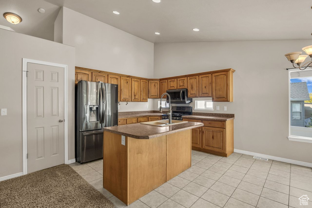 Kitchen featuring appliances with stainless steel finishes, high vaulted ceiling, light tile patterned floors, a kitchen island with sink, and brown cabinetry