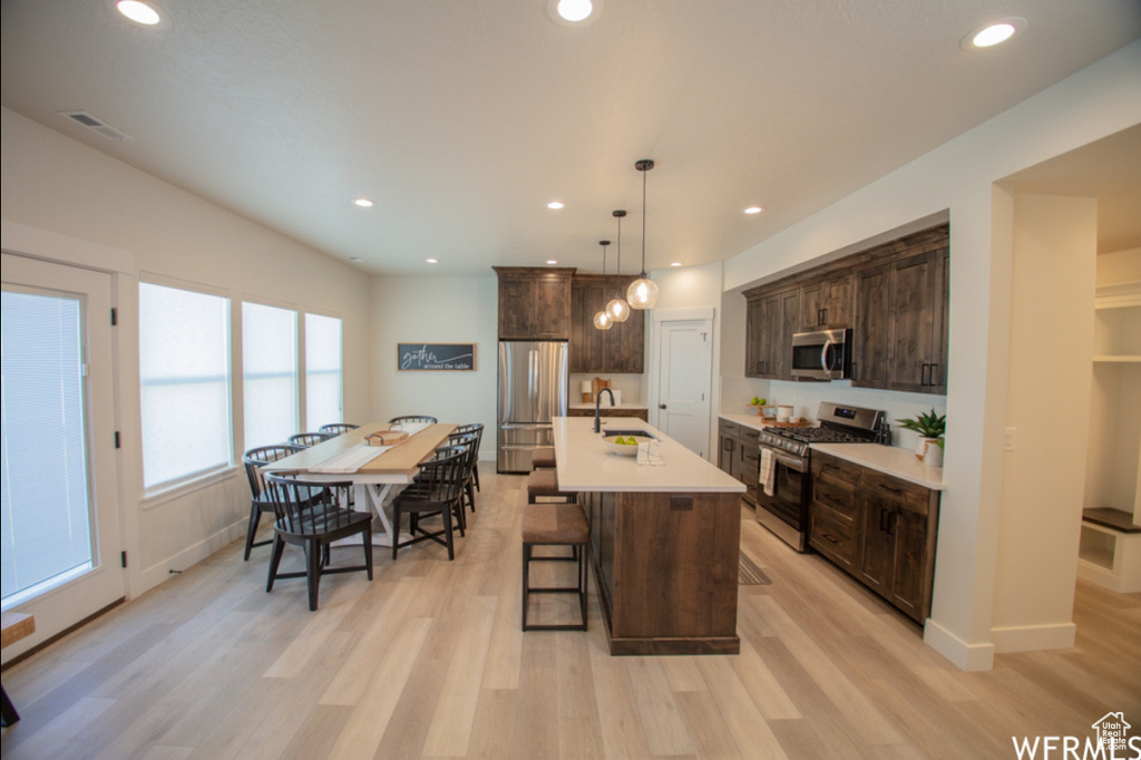 Kitchen with appliances with stainless steel finishes, a kitchen bar, dark brown cabinets, light wood-type flooring, and recessed lighting
