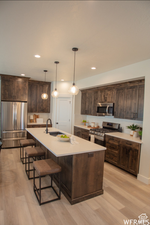 Kitchen with appliances with stainless steel finishes, light wood finished floors, a breakfast bar, dark brown cabinetry, and recessed lighting