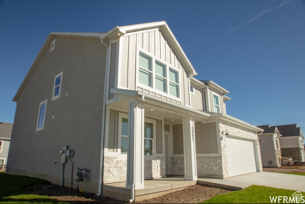 View of front of home with a porch, driveway, a garage, board and batten siding, and stone siding