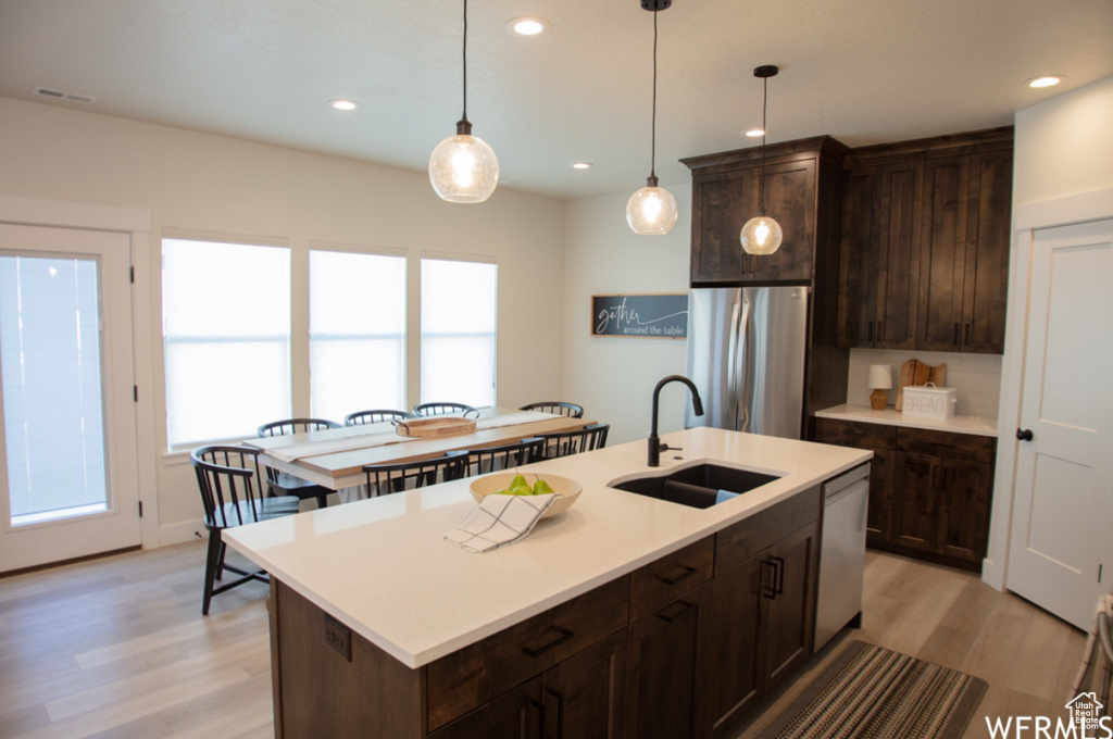 Kitchen with stainless steel appliances, plenty of natural light, light wood finished floors, dark brown cabinetry, and recessed lighting