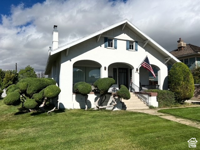 View of front of property with covered porch, a front lawn, a chimney, and stucco siding