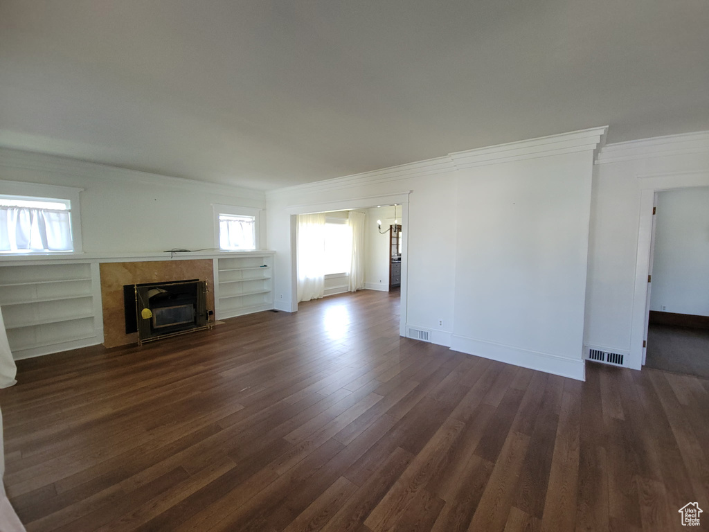 Unfurnished living room featuring ornamental molding, plenty of natural light, dark wood-type flooring, a premium fireplace, and a chandelier