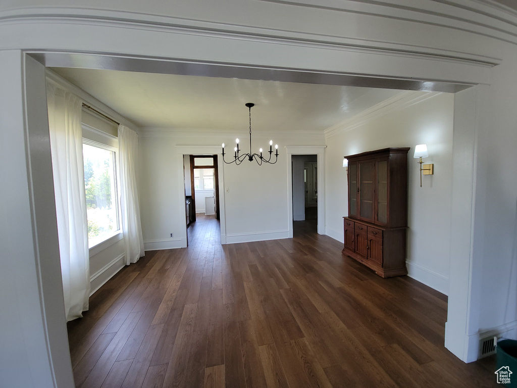 Unfurnished dining area featuring a chandelier, dark wood finished floors, and crown molding