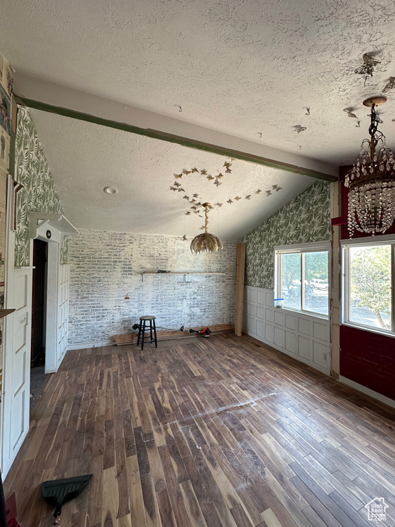 Unfurnished living room with dark wood finished floors, a textured ceiling, a wainscoted wall, and a chandelier