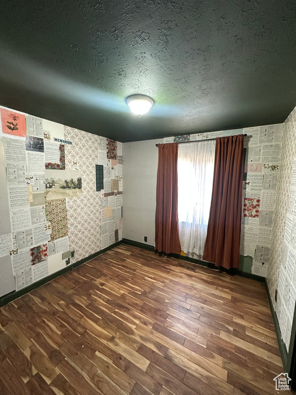 Unfurnished room featuring wood finished floors, a textured ceiling, and wallpapered walls