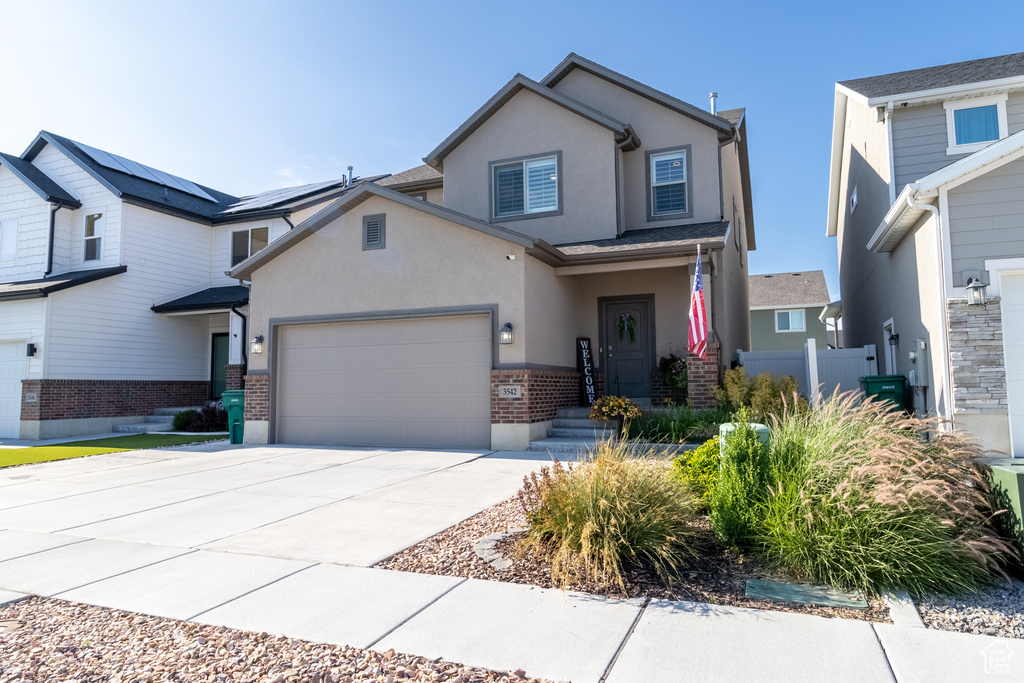 View of front of house with stucco siding, driveway, brick siding, and a garage