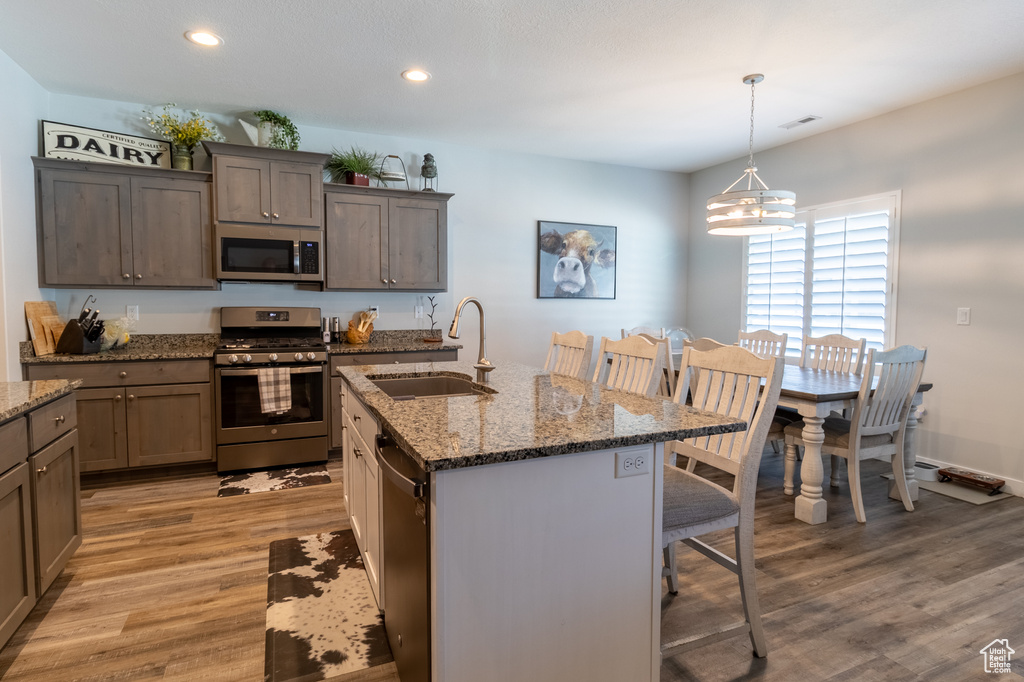 Kitchen featuring appliances with stainless steel finishes, a kitchen breakfast bar, light wood-type flooring, a chandelier, and stone counters