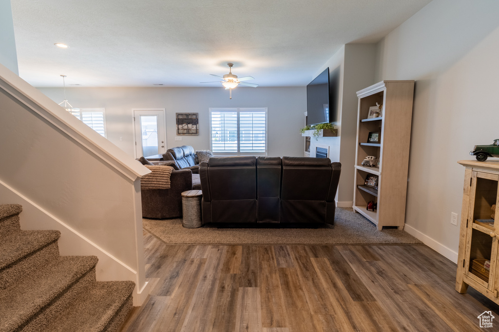 Living area with wood finished floors, ceiling fan, stairs, and a glass covered fireplace