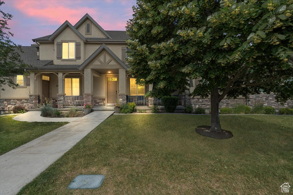 View of front of home featuring stucco siding, stone siding, a porch, and a yard