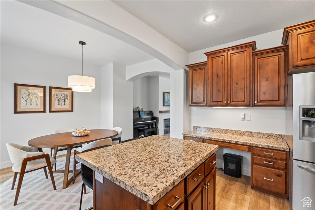 Kitchen featuring stainless steel fridge with ice dispenser, arched walkways, light wood-type flooring, light stone countertops, and recessed lighting