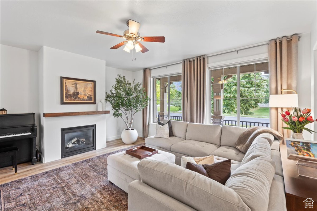 Living room with a glass covered fireplace, a ceiling fan, and wood finished floors
