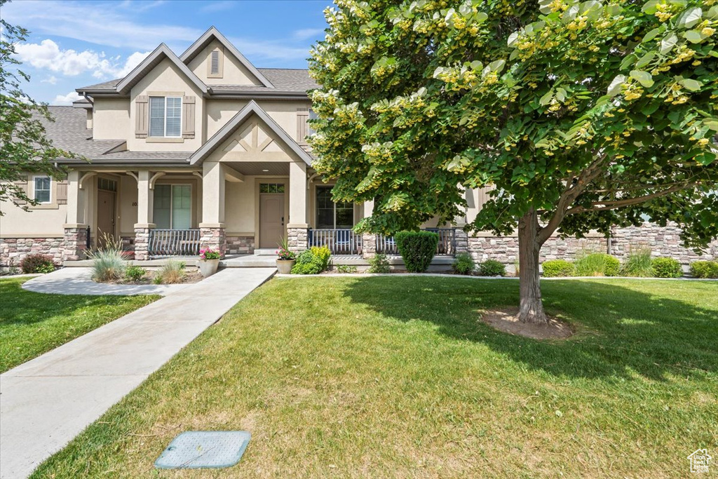 Craftsman inspired home featuring stucco siding, covered porch, stone siding, and a front lawn