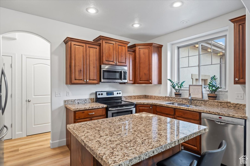 Kitchen with appliances with stainless steel finishes, light wood-style flooring, a breakfast bar, a center island, and light stone counters