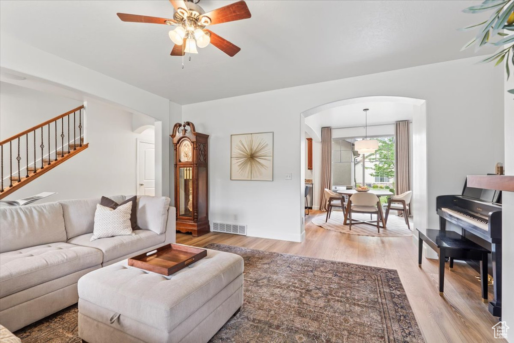 Living area featuring arched walkways, light wood finished floors, ceiling fan, and stairs