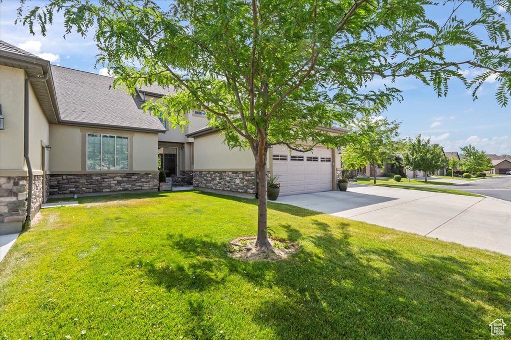 View of front facade featuring stucco siding, driveway, stone siding, and a front lawn