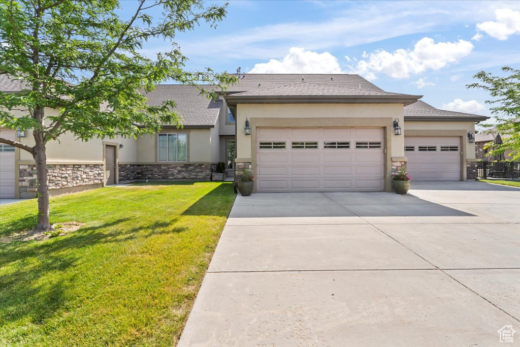 View of front of house featuring stucco siding, driveway, an attached garage, stone siding, and a front lawn