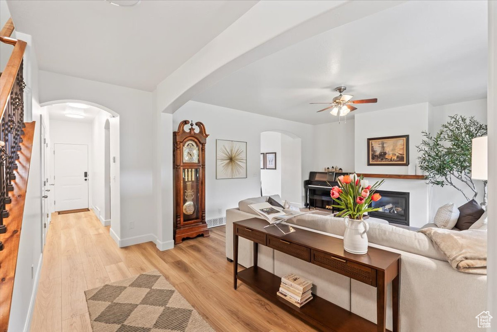 Living room with arched walkways, light wood-type flooring, ceiling fan, and stairway