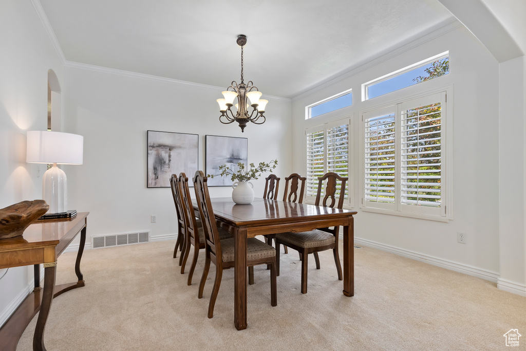 Dining room featuring a chandelier, light colored carpet, crown molding, and arched walkways