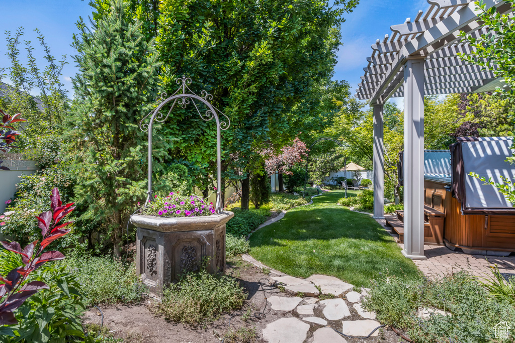 View of grassy yard with a pergola and a hot tub