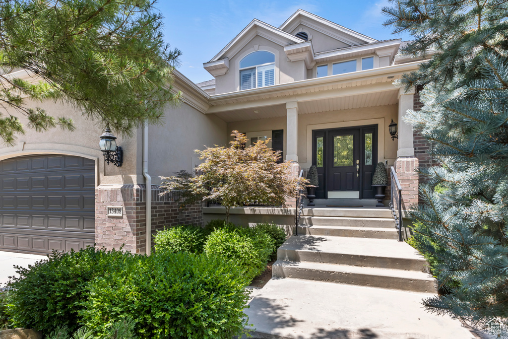 Entrance to property with stucco siding, an attached garage, and a porch