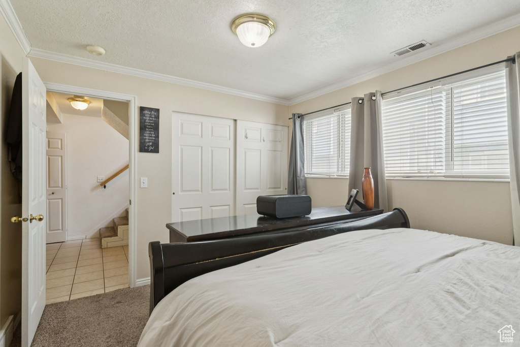 Carpeted bedroom with tile patterned floors, ornamental molding, a closet, and a textured ceiling
