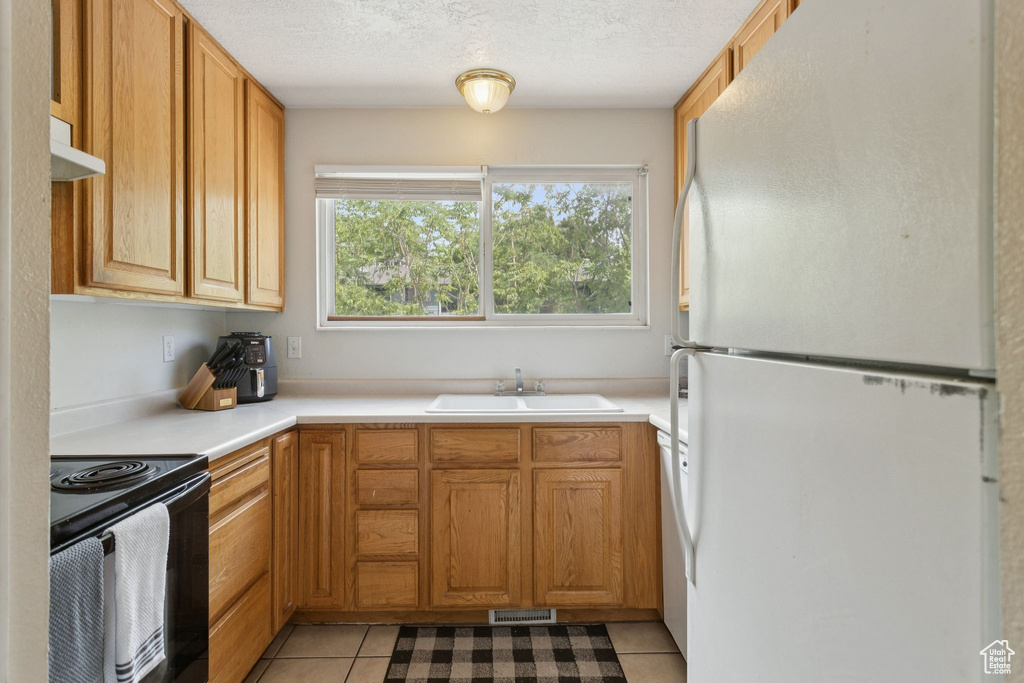 Kitchen featuring freestanding refrigerator, black electric range, light tile patterned floors, light countertops, and ventilation hood