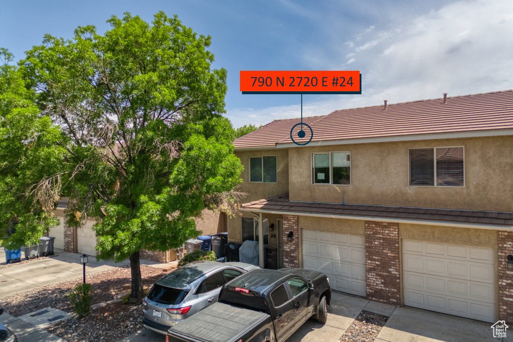 Townhome / multi-family property with brick siding, stucco siding, driveway, and an attached garage