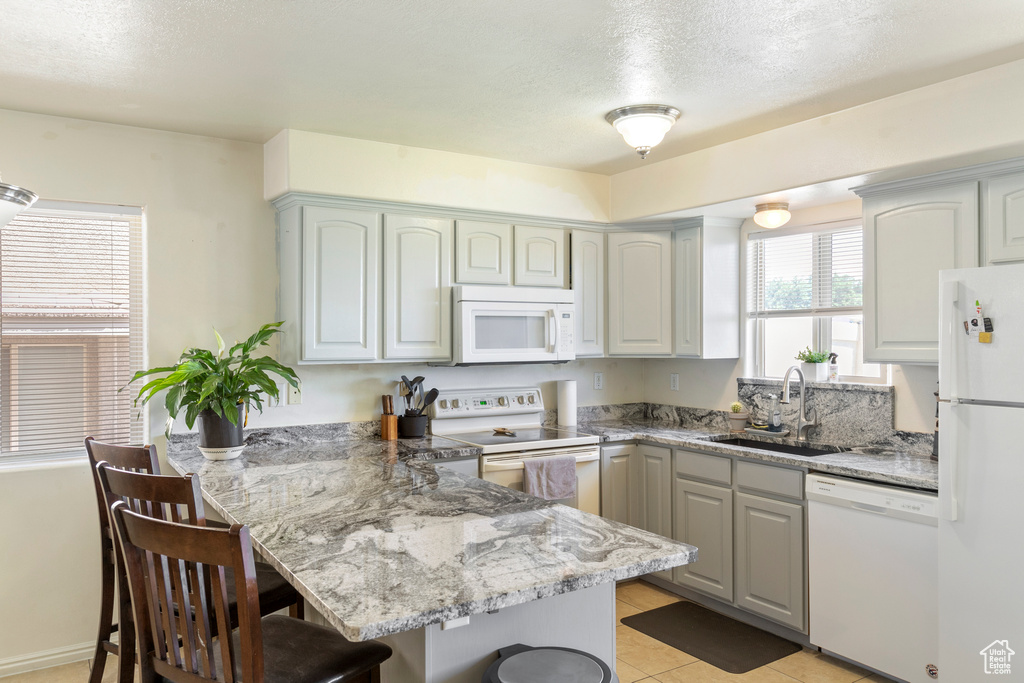 Kitchen with white appliances, a peninsula, a breakfast bar, light stone counters, and light tile patterned floors