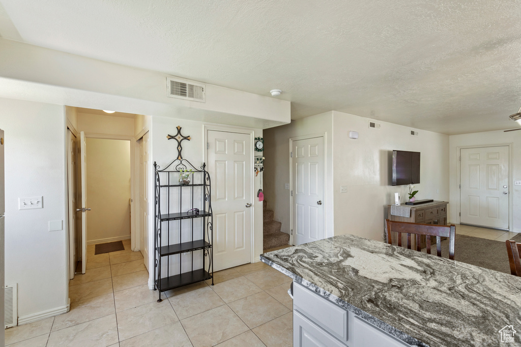 Kitchen with a textured ceiling, light tile patterned flooring, and stone counters