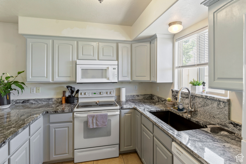 Kitchen featuring white appliances, light tile patterned floors, and stone counters