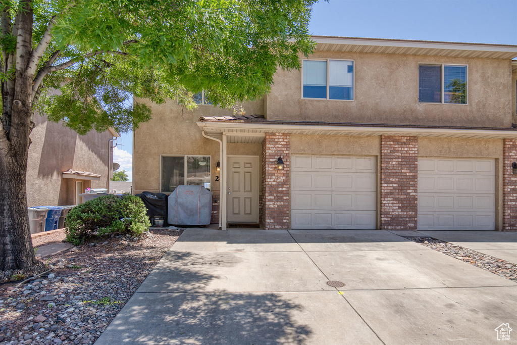 View of front of property featuring driveway, stucco siding, a garage, and brick siding