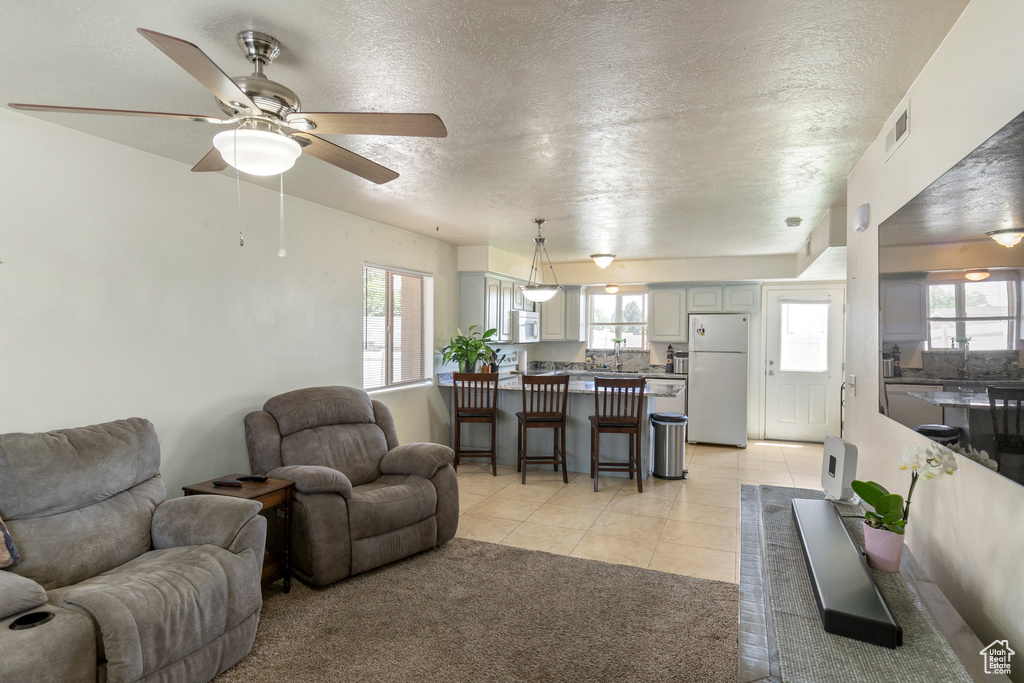 Living area with a textured ceiling, healthy amount of natural light, a ceiling fan, and light tile patterned floors