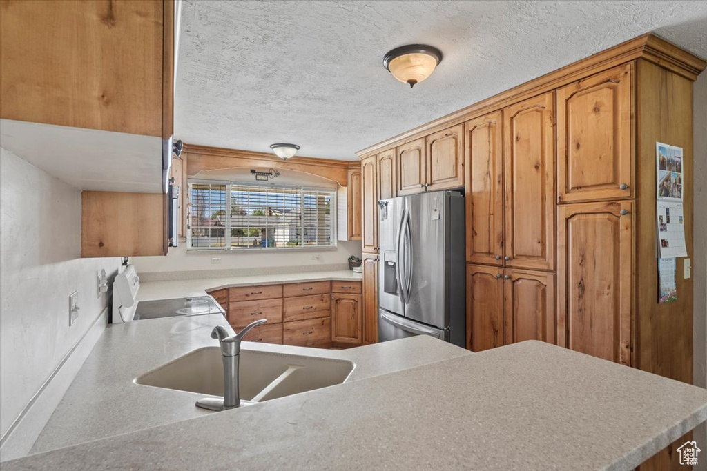 Kitchen featuring stainless steel refrigerator with ice dispenser, electric range oven, a textured ceiling, light countertops, and brown cabinetry