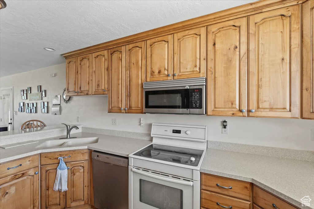 Kitchen with appliances with stainless steel finishes, light countertops, a textured ceiling, a peninsula, and recessed lighting