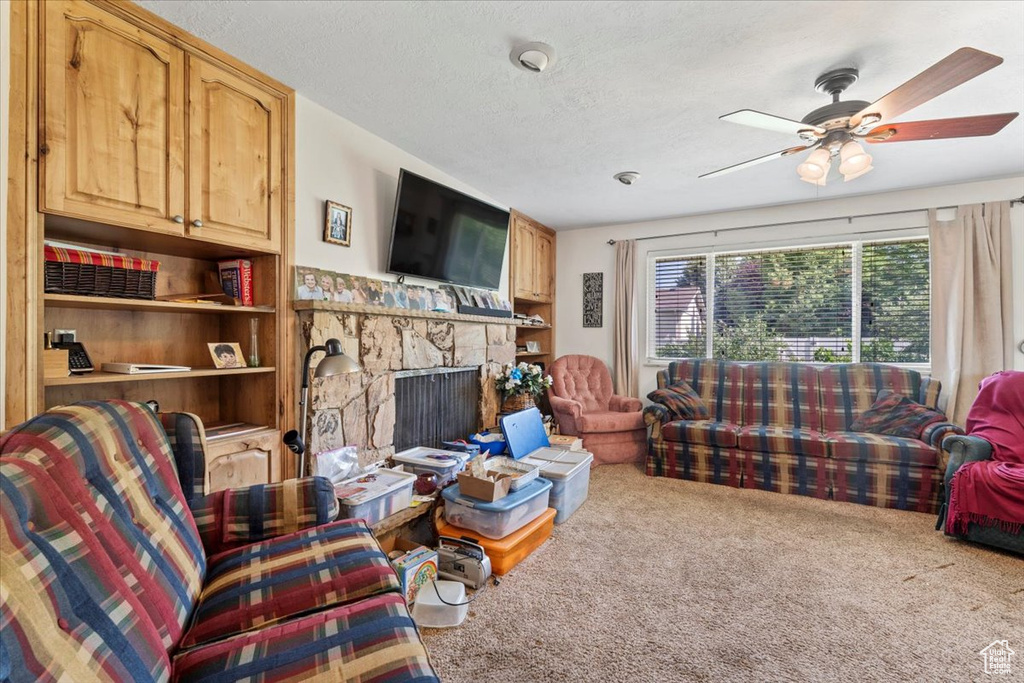 Living area with carpet flooring, ceiling fan, a fireplace, and a textured ceiling