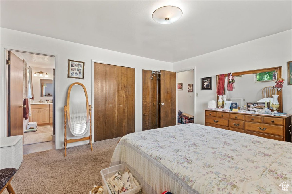 Bedroom with multiple closets, light carpet, and ensuite bathroom