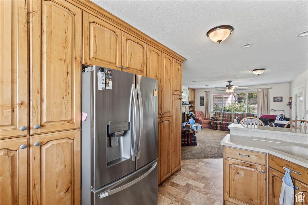 Kitchen featuring stainless steel refrigerator with ice dispenser, ceiling fan, open floor plan, light countertops, and light carpet