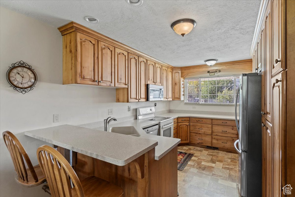 Kitchen with appliances with stainless steel finishes, a peninsula, a kitchen breakfast bar, a textured ceiling, and light countertops