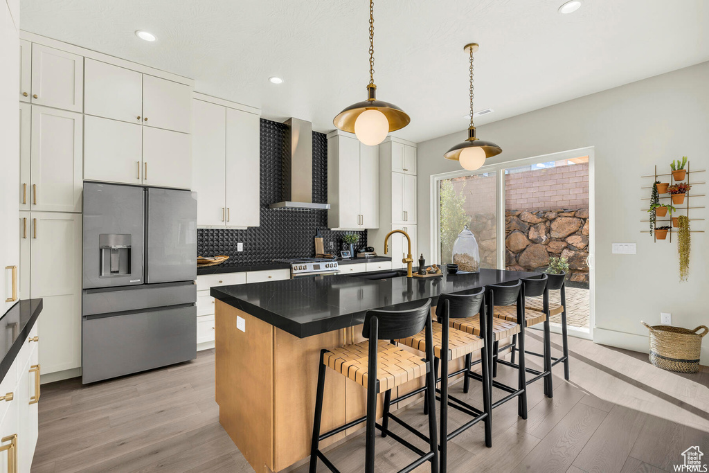 Kitchen with appliances with stainless steel finishes, wall chimney exhaust hood, light wood finished floors, tasteful backsplash, and recessed lighting